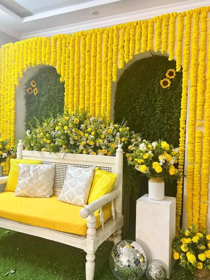 A bright and sunny Haldi ceremony setup. The contrast of the yellow marigold arches against the green foliage wall creates a fresh and vibrant look, perfect for a daytime celebration.