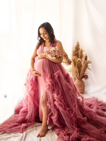 A gentle portrait of an expecting mother in a pink gown, holding a bouquet and looking down at her bump with love.