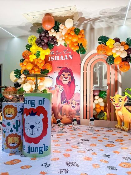 A 'King of the Jungle' Lion King theme for a first birthday. This setup includes arched backdrops, character cutouts of Simba, and a balloon garland in warm, earthy tones.