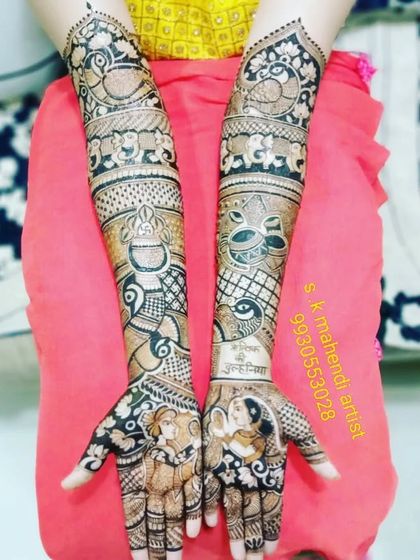 This design includes portraits of the couple on the palms. The arms are decorated with peacocks, elephants, and kalash motifs, creating a full bridal look.