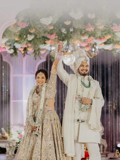 A triumphant and happy moment after the wedding ceremony, with the couple raising their hands in celebration under a canopy of flowers.