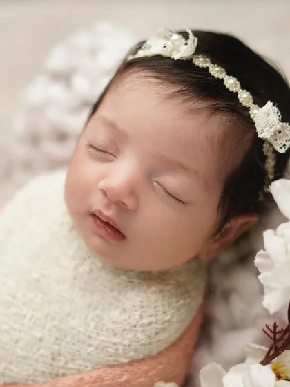 A sweet close-up of a newborn's face, framed by white flowers. The focus on her delicate features and lace headband makes for a truly precious memory.