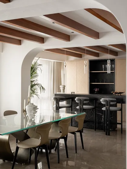 A well-designed dining and bar area becomes the heart of the home. Here, I combined a sleek glass dining table with a dark marble bar and exposed wooden ceiling beams to balance modern elegance with a warm, earthy feel, perfect for entertaining.