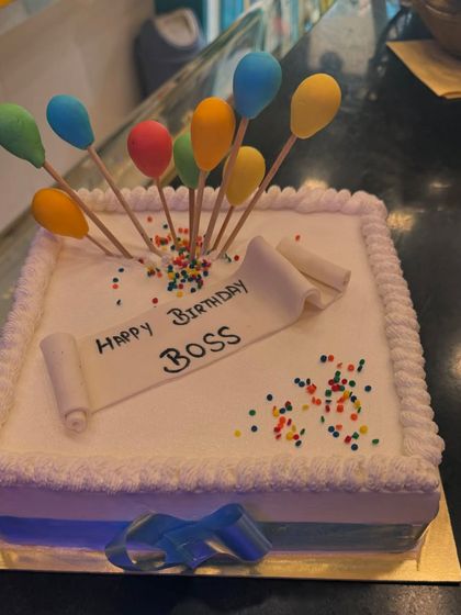 A simple and respectful birthday cake for a boss. The design is clean, with a "Happy Birthday Boss" message on a fondant scroll and colorful balloon toppers.