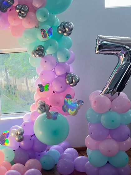 A closer look at the butterfly theme balloon pillar and arch. The mix of pastel pink, purple, and mint green balloons with silver accents creates a magical look for a girl's birthday.
