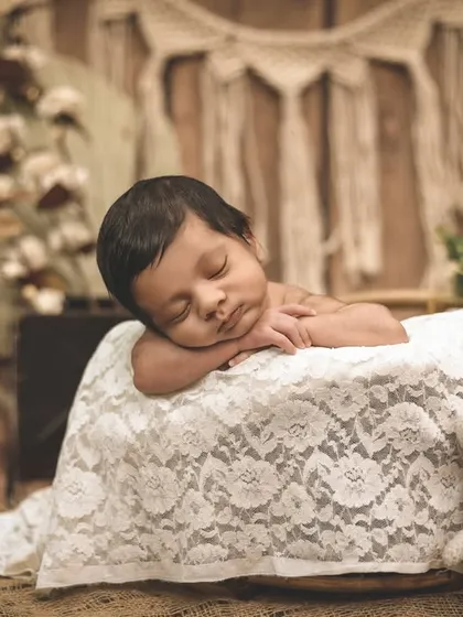 A full-length view of the sleeping newborn in a boho setup. The natural textures of wood, jute, and dried plants create a warm and calming atmosphere.