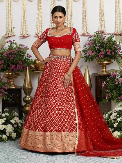 The regal posture of the model highlights the majestic fall of this red bridal lehenga. The wide golden zari border adds a touch of opulence, perfect for a grand wedding ceremony.