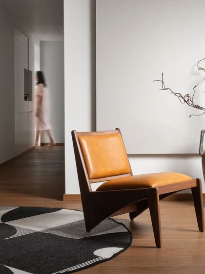 A beautifully crafted wooden chair with tan leather upholstery stands as a sculptural object in this minimalist interior by Aakriti Saraf Design.