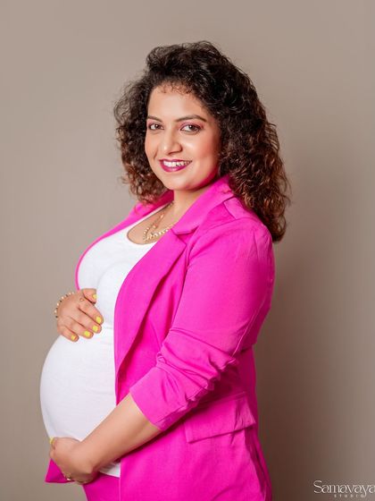 A happy and bright portrait of an expecting mother in a chic pink blazer. This look is perfect for a contemporary and stylish studio session.