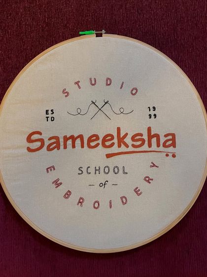 The finished hand-embroidered logo for Sameeksha School of Embroidery, mounted in a hoop. It is a symbol of our dedication to this beautiful craft.