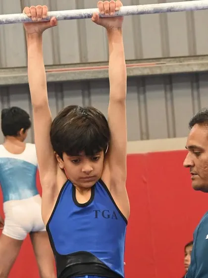 A coach watches intently as a young gymnast practices on the low bar, demonstrating our commitment to focused training.