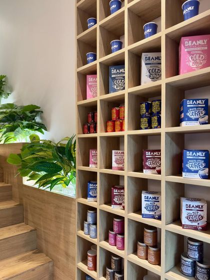 A detail of the floor-to-ceiling merchandising shelf at Beanly. The simple wooden grid provides a neutral background that makes the brand's colorful packaging stand out, turning the product display into a major design feature.