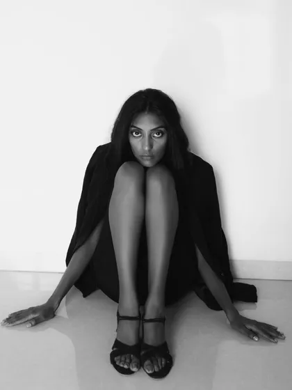 A striking black and white portrait with a strong graphic quality. The model's pose, crouched on the floor, is unconventional and creates a powerful, angular composition.
