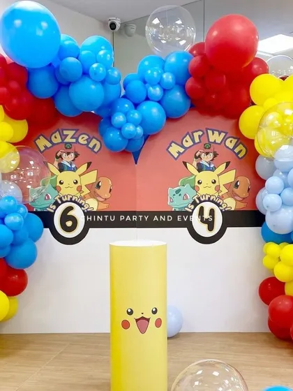 A Pokemon themed birthday decoration for two brothers. The shared backdrop features Ash, Pikachu, and other characters, framed by a colorful balloon arch.