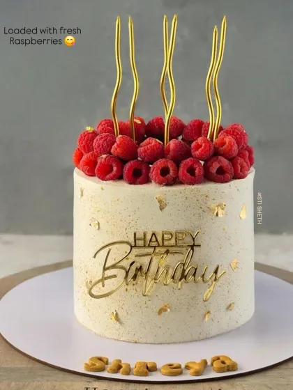A stunning cake piled high with fresh raspberries and accented with gold candles and a "Happy Birthday" topper.
