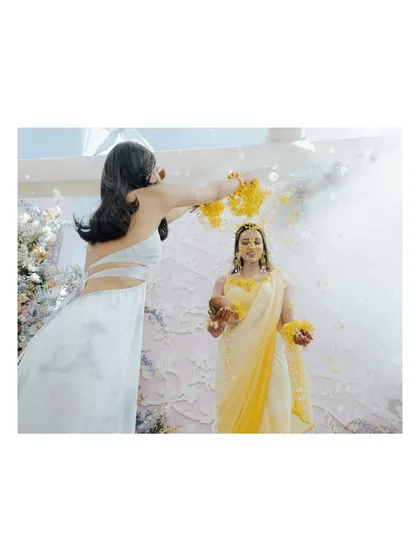 A friend showers the bride with flower petals during her haldi, a beautiful and joyous moment of celebration.