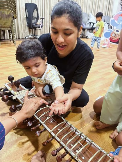 A parent helps their child gently touch the strings of a sitar. Our workshops are designed to be a shared experience, where families can discover the beauty of Indian instruments together.