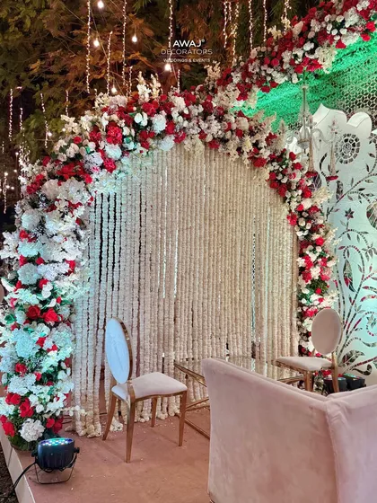 A close-up of the Nikah ceremony backdrop, featuring a curtain of white flowers (rajanigandha) framed by a lush arch of red and white roses.