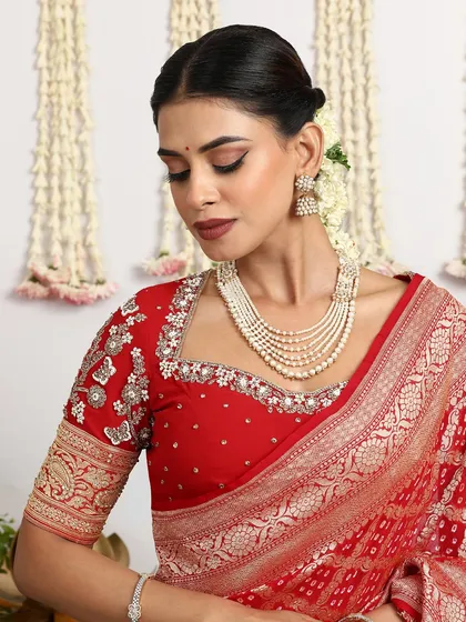 A close-up of a beautiful red Banarasi Bandhani saree, paired with a heavily embroidered blouse.