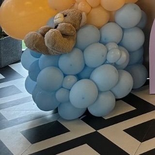 A small teddy bear resting on a cloud of light blue balloons, showcasing the detailed and thoughtful placement of props.