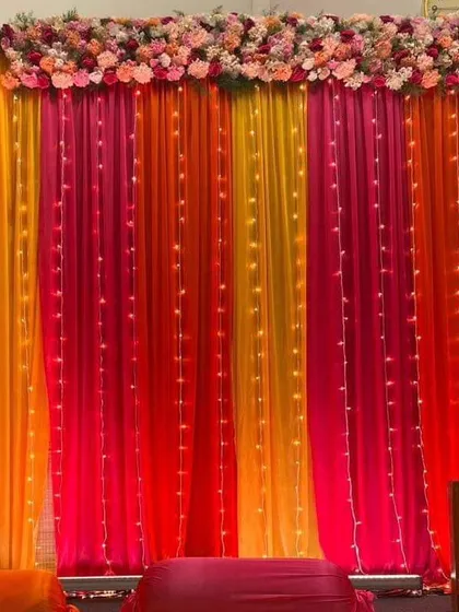 A vibrant backdrop of orange, pink, and yellow drapes with fairy lights. This simple yet effective design is perfect for adding a pop of color to any celebration.