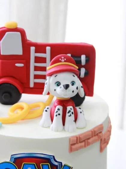 A close-up of the handcrafted Marshall topper, complete with his firefighter helmet, sitting next to his fire truck on the Paw Patrol cake.
