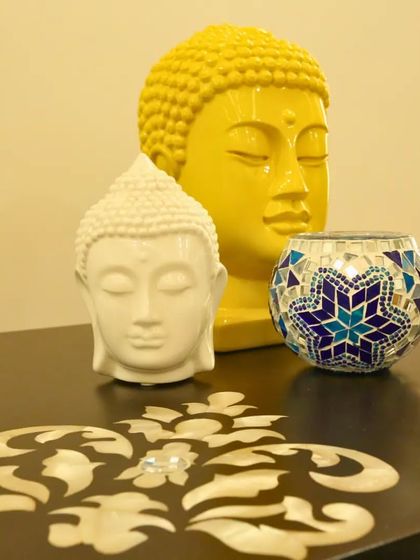 Even small decor items can bring a spiritual touch. Here, two Buddha heads in contrasting yellow and white are paired with a mosaic candle holder, creating a simple yet peaceful arrangement on a tabletop.