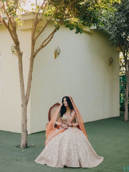 A regal bridal portrait, with the bride seated gracefully on a chair in a lush green lawn, looking like modern royalty.