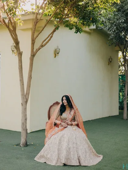 A regal bridal portrait, with the bride seated gracefully on a chair in a lush green lawn, looking like modern royalty.