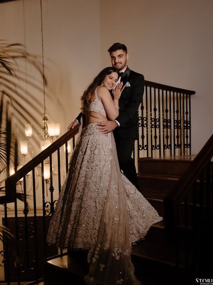 A classic, elegant portrait of Navya and Rishi on a staircase, showcasing their glamorous engagement outfits.