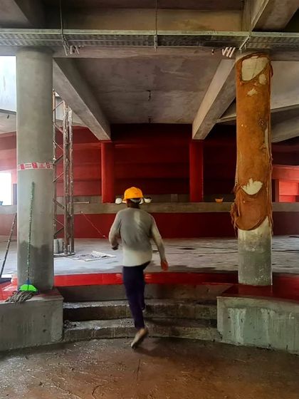 A worker moving through the unfinished space of the TAPMI Centre, giving a sense of scale to the raw, red-plastered interiors.