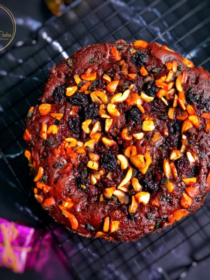 An overhead shot of the classic round Christmas plum cake. The top is generously covered with a mix of cashews, almonds, and raisins, providing a delightful crunch and sweetness.