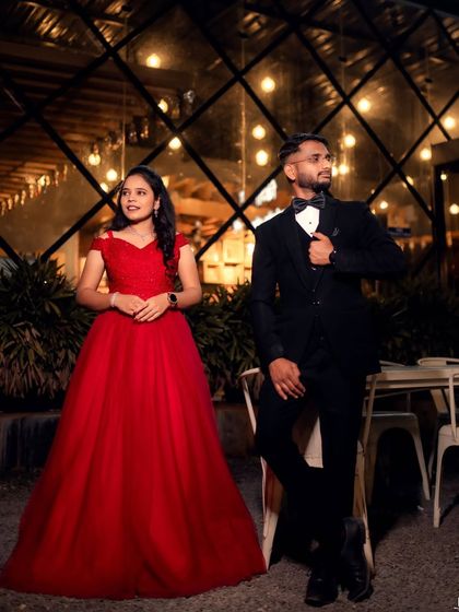 A chic and modern couple's portrait. The string lights in the background add a magical glow to this pre-wedding photo, highlighting the classic red gown and tuxedo.