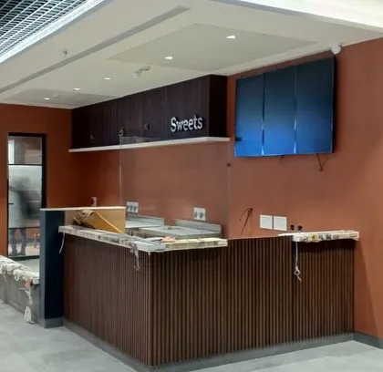 A construction shot of the service counter area at Haldiram's Pitampura. The warm, rust-colored wall and the wood-paneled counters are being installed, bringing the concept render to life.