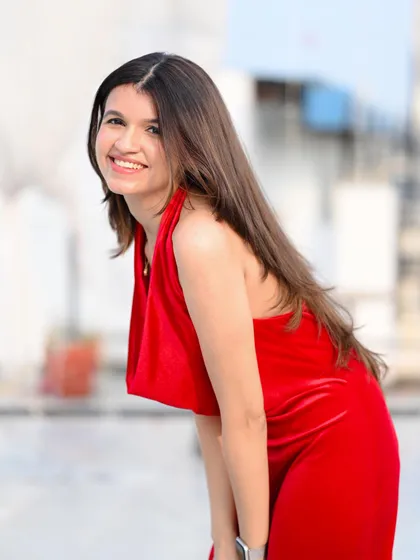 A happy and radiant portrait of a model in a red velvet dress, shot on a rooftop with a blurred city background.