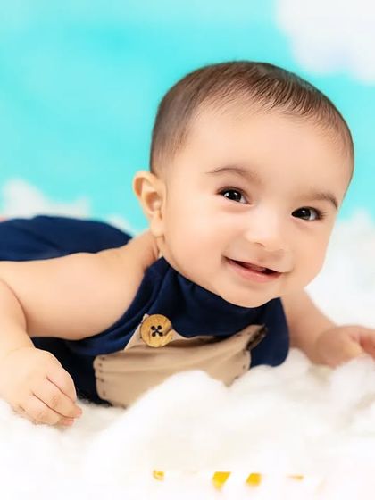 A happy baby boy lies on a bed of clouds, looking up with a bright smile. A dreamy and imaginative portrait.