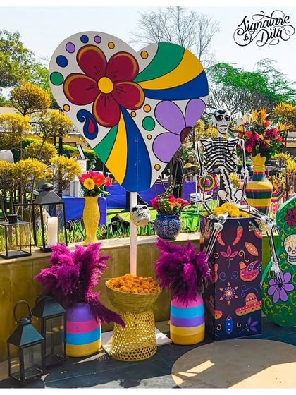 This vignette combines a colorful heart-shaped prop, a skeleton, and vibrant floral arrangements in painted vases, showcasing the theme's playful take on 'Day of the Dead' iconography.