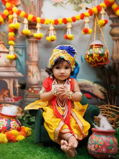 A serene portrait of a baby dressed as little Krishna, sitting peacefully in a vibrant, festive setup.