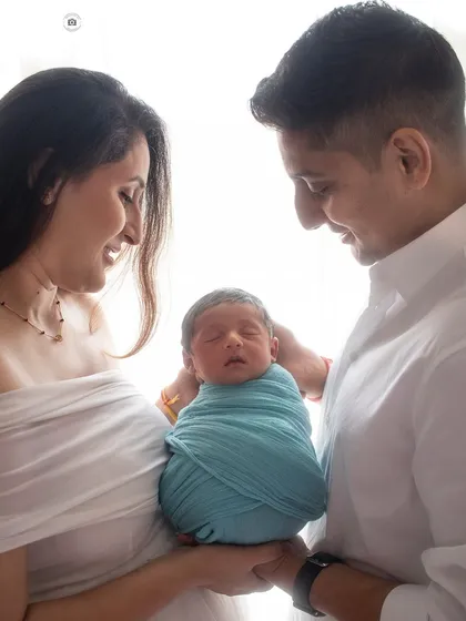 Welcoming their newborn with so much love. The parents' adoring smiles and the baby peacefully wrapped in blue create a perfect first family photo.
