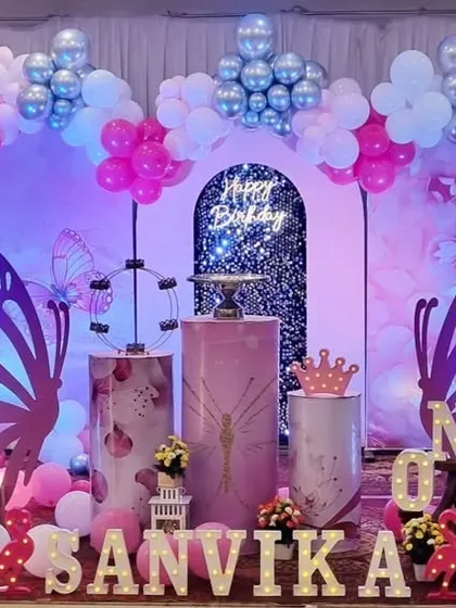 A stunning butterfly-themed first birthday setup with a shimmer wall backdrop, large marquee 'ONE', and beautiful pink and silver balloon decorations.
