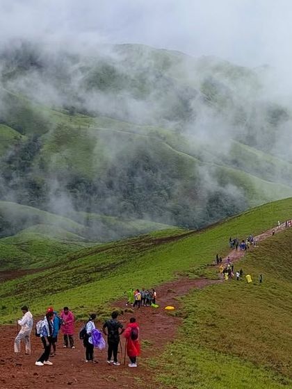 A wide shot of the famous Nethravathi trail snaking along the mountain ridge, dotted with trekkers making their way up.