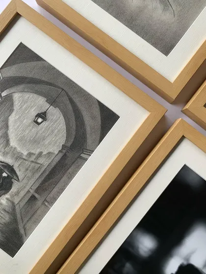 A collection of sketches in matching maple frames, creating a warm and cohesive gallery display. The consistent framing style unifies the different artworks.
