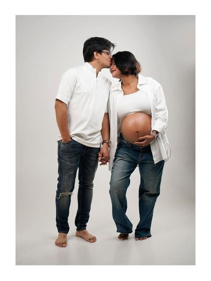 A standing portrait of a couple in casual jeans and white shirts, holding hands and sharing a sweet moment.