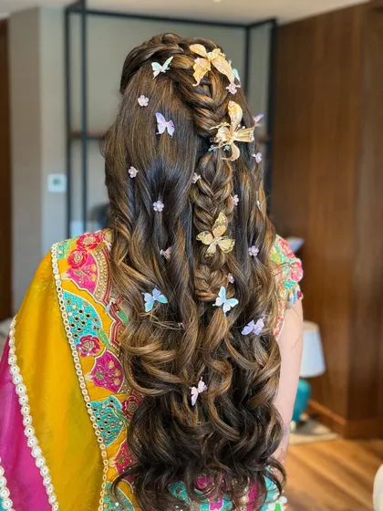For a playful and whimsical Mehandi look, I created this half-up, half-down style featuring a fishtail braid and voluminous curls. The look is brought to life with an array of delicate butterfly clips in gold and pastel shades, adding a touch of magic.