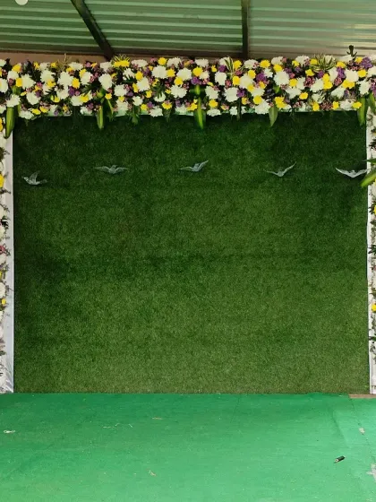 A simple yet elegant Shreemantha backdrop using a green wall framed by a fresh floral arch. This is a great option for a clean and natural look.