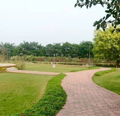 A serene park setting with a paved walkway curving through a well-maintained lawn. Our designs for public parks prioritize open space, healthy turf, and strategic tree planting for shade and beauty.