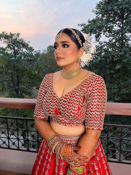 A radiant and resplendent Indian bride. This look captures timeless beauty with makeup that complements her traditional red attire, making her shine on her special day.