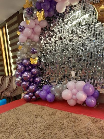 A close-up of a 40th anniversary decoration featuring a stunning silver shimmer wall. The purple, lavender, and silver balloon garland with golden butterfly accents adds a touch of glamour.