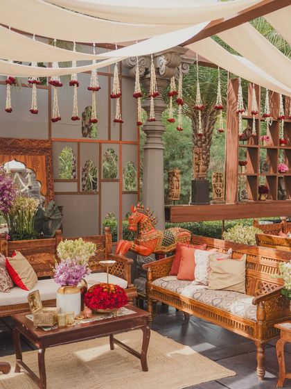 A cozy lounge area with carved wooden sofas, colorful cushions, and hanging floral strings, inspired by the charm of an artisan's studio.