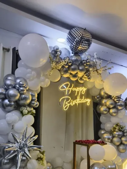 A glamorous silver and white balloon arch with disco ball accents. This setup, complete with a neon sign, is perfect for a dance party or a disco-themed birthday.